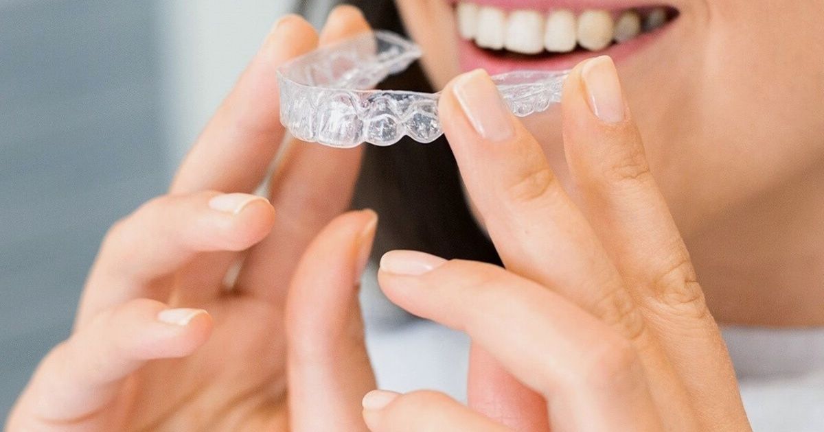 Woman holding a clear Invisalign aligner tray up in front of her smile